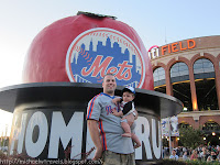 a man holding a baby in front of a large baseball sign