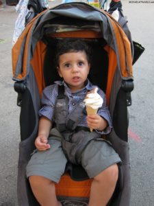 a baby sitting in a stroller eating an ice cream cone
