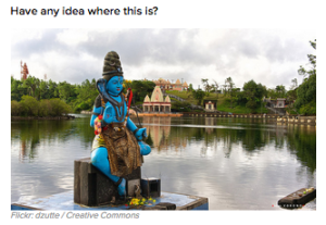 a statue of a blue god sitting on a platform next to a body of water