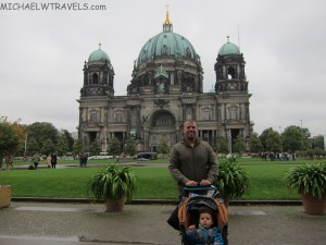a man pushing a stroller in front of a large building with Berlin Cathedral in the background