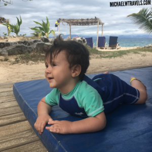 a baby lying on a blue mat on a beach