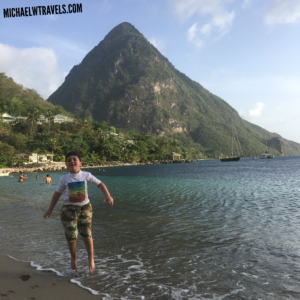 a boy standing on the beach with Pitons in the background