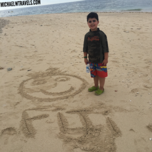 a boy standing in the sand with a smiley face drawn in the sand