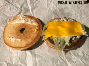 a burger with cheese and lettuce on top of a bagel
