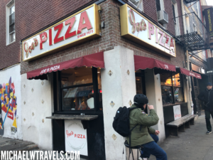 a person sitting on a stool outside of a pizza restaurant