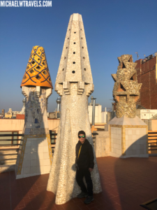 a man standing in front of a tall white and yellow tower with Palau Güell in the background