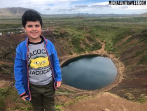 a boy standing on a hill with a lake in the background
