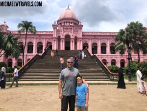 a man and a child posing for a picture in front of a pink building with Ahsan Manzil in the background