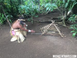 a man sitting on the ground near a structure made of sticks