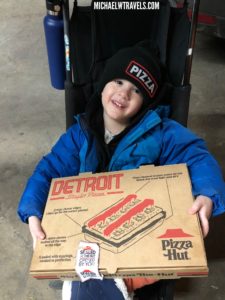 a boy in a blue coat holding a pizza box