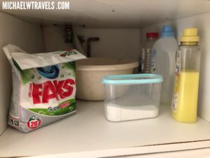a shelf with a container of washing powder and a bowl