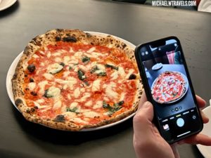 a hand holding a phone taking a picture of a pizza