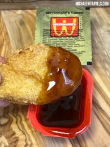 a hand holding a fried chicken with sauce in a red container