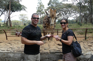 a man and woman standing in front of a giraffe