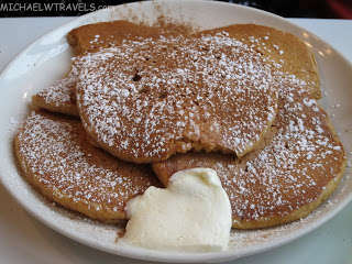 a plate of pancakes with icing sugar and whipped cream