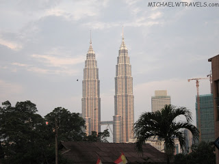 a tall buildings with trees in the background with Petronas Towers in the background