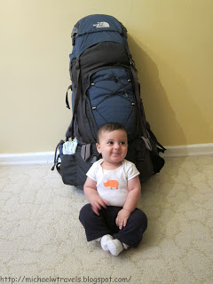 a baby sitting next to a large backpack