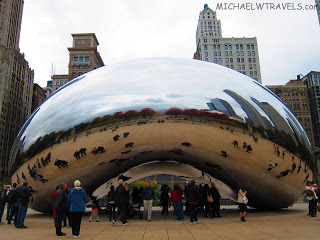 a group of people standing around a large reflective object with Millennium Park in the background