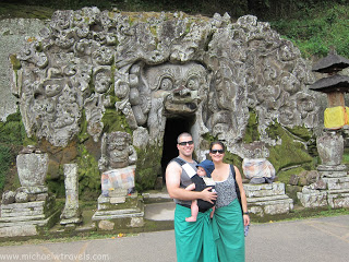 a man and woman holding a baby in front of a carved rock structure