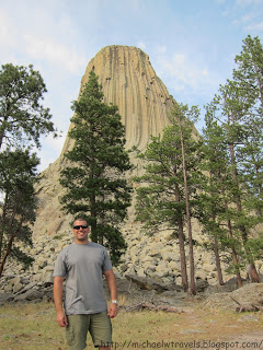 a man standing in front of a tall rock formation with Devils Tower in the background