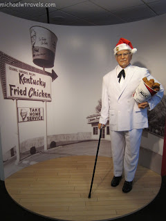 a wax figure of a man wearing a santa hat and holding a bucket of chicken