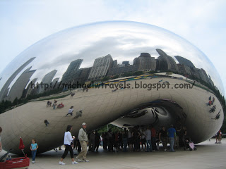 a group of people walking around a reflective sculpture with Millennium Park in the background