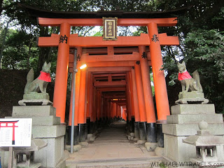 a long tunnel with orange pillars with Fushimi Inari-taisha in the background