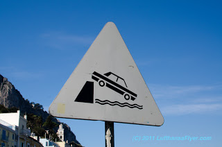 a triangular sign with a car falling off a cliff