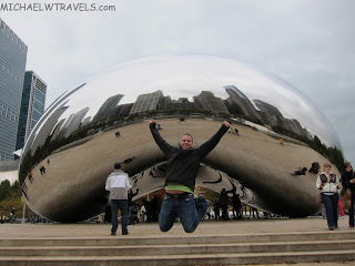 a man jumping in the air in front of a reflective bean with Millennium Park in the background