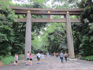 a group of people walking under a large wooden arch with Meiji Shrine in the background