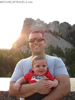 a man holding a baby in front of mount rushmore