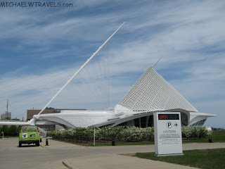 a white building with a triangular roof with Milwaukee Art Museum in the background