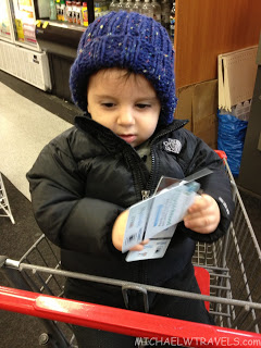a child in a blue hat and coat holding a ticket in a shopping cart