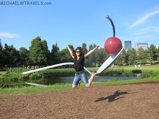 a woman jumping in the air with a cherry and a statue with Minneapolis Sculpture Garden in the background