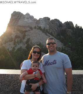 a man and woman with a baby in front of mount rushmore
